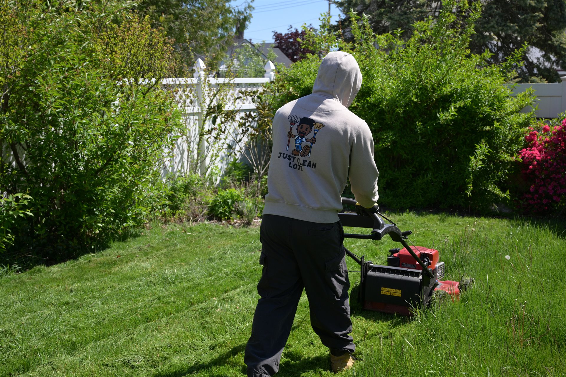 JCL crew member in branded hoodie mowing a lawn with a Honda push mower